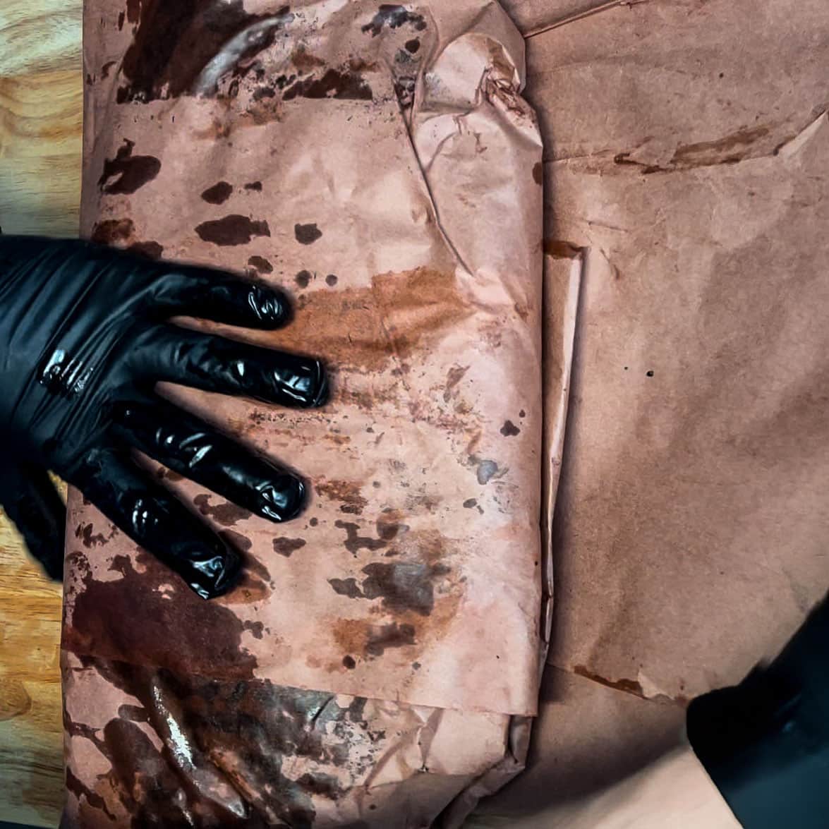 Brisket being wrapped tightly in pink butcher paper