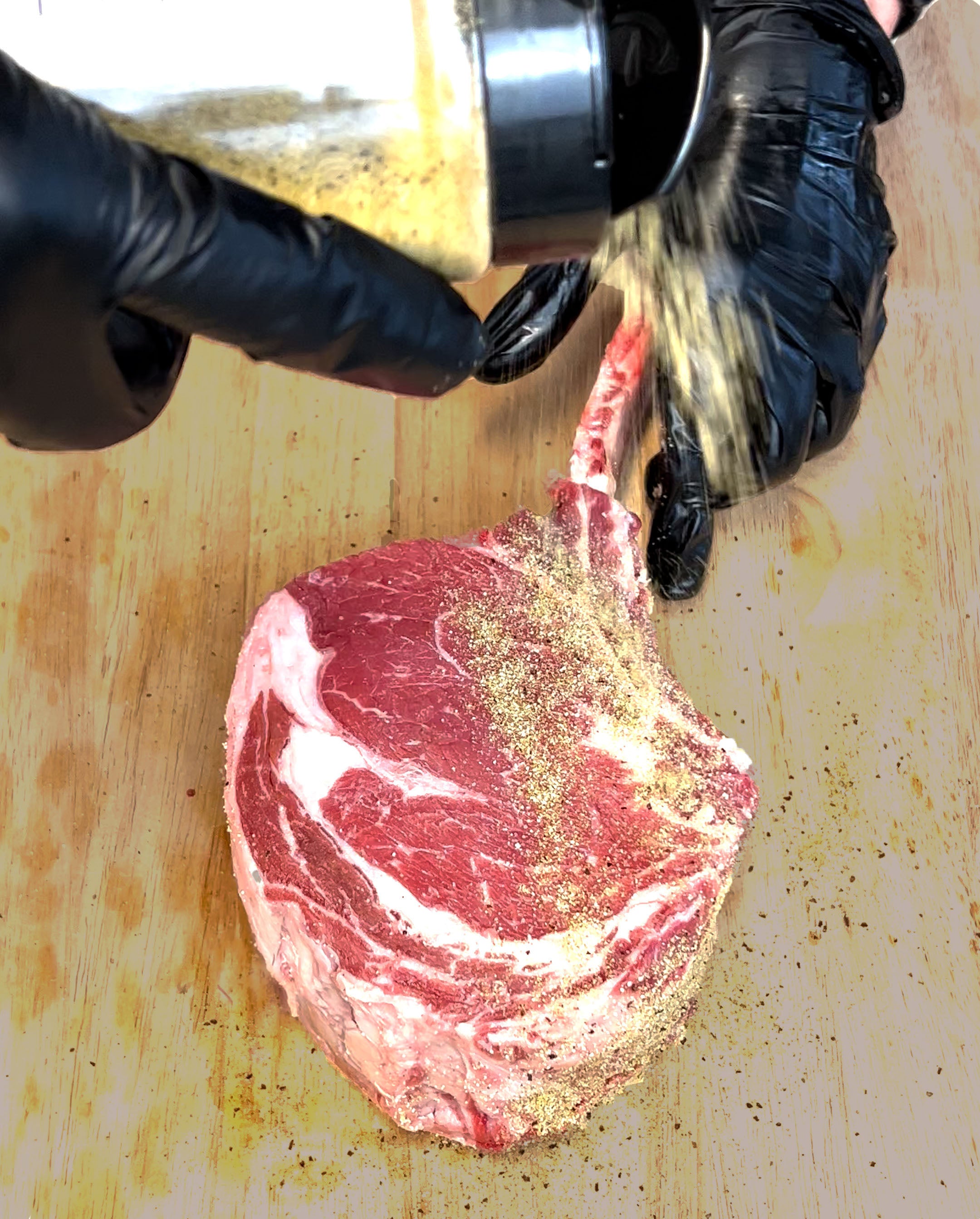 Tomahawk ribeye steak being seasoned with Sure Fire BBQ Garlic Jalapeño rub