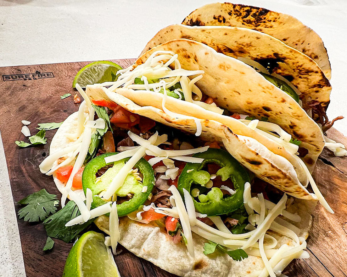 Shredded beef tacos with condiments on a wooden platter