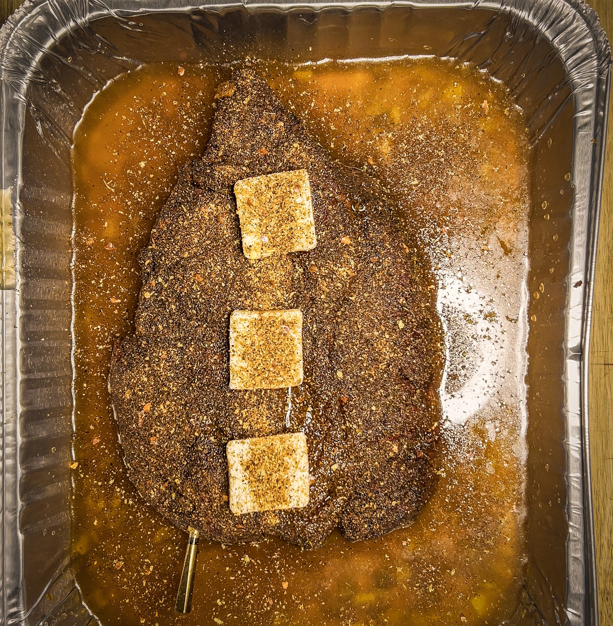Beef chuck roast in a half sheet pan with butter, seasoning, and beef broth being wrapped tightly